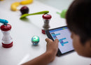 Young boy programming mini robotic ball in between a salt and pepper shaker.